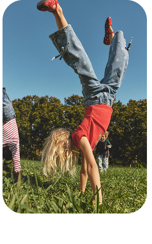Young girl doing a handstand on grass wearing red shirt and jeans