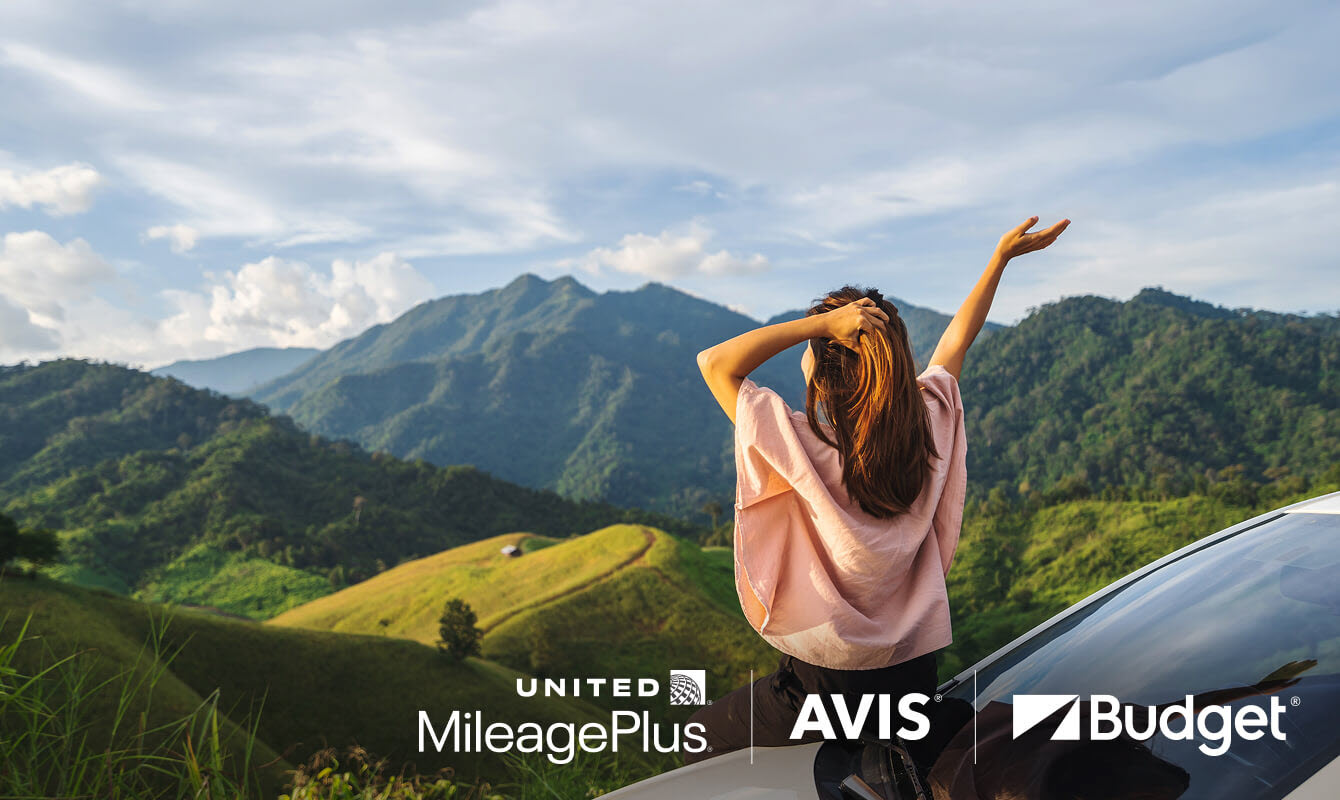 A person looks out over the mountains standing next to a car.