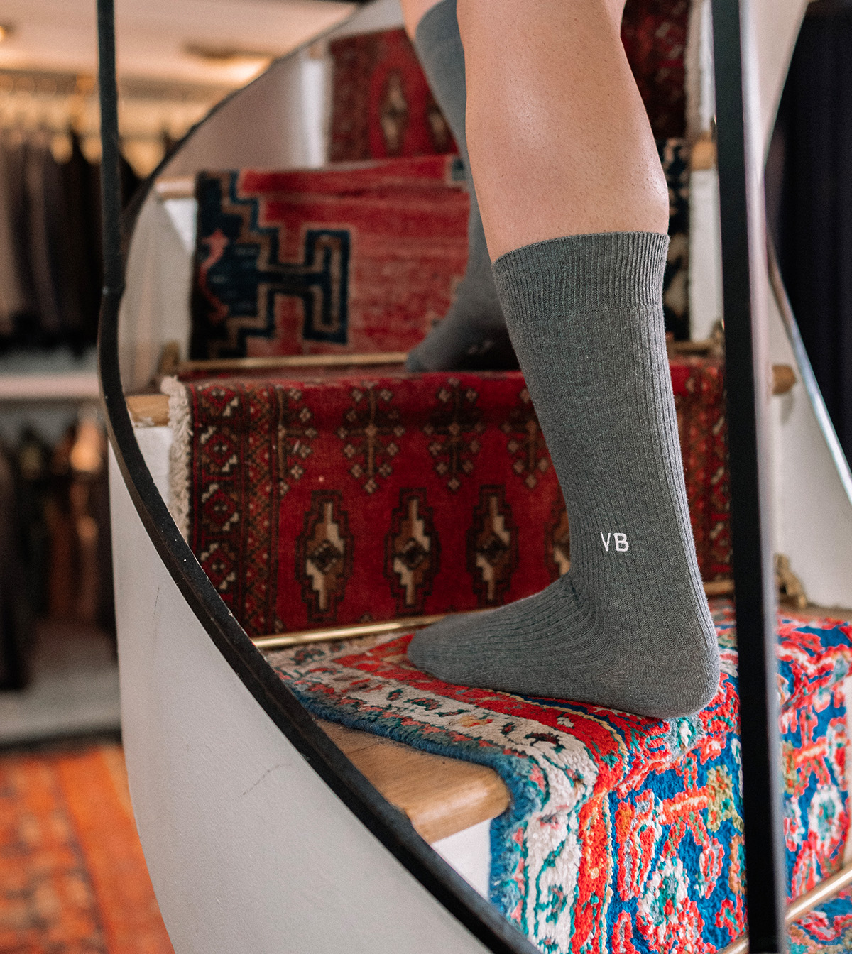 man walking up a staircase wearing grey dress socks with letters VB monogrammed.