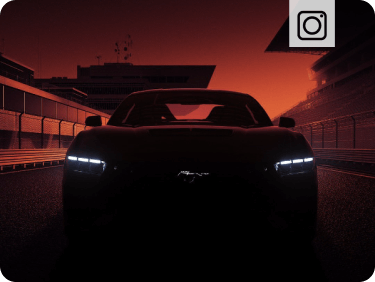 Front‑facing view of a Ford Mustang&reg; vehicle with illuminated headlamps and a dark orange sky in the background