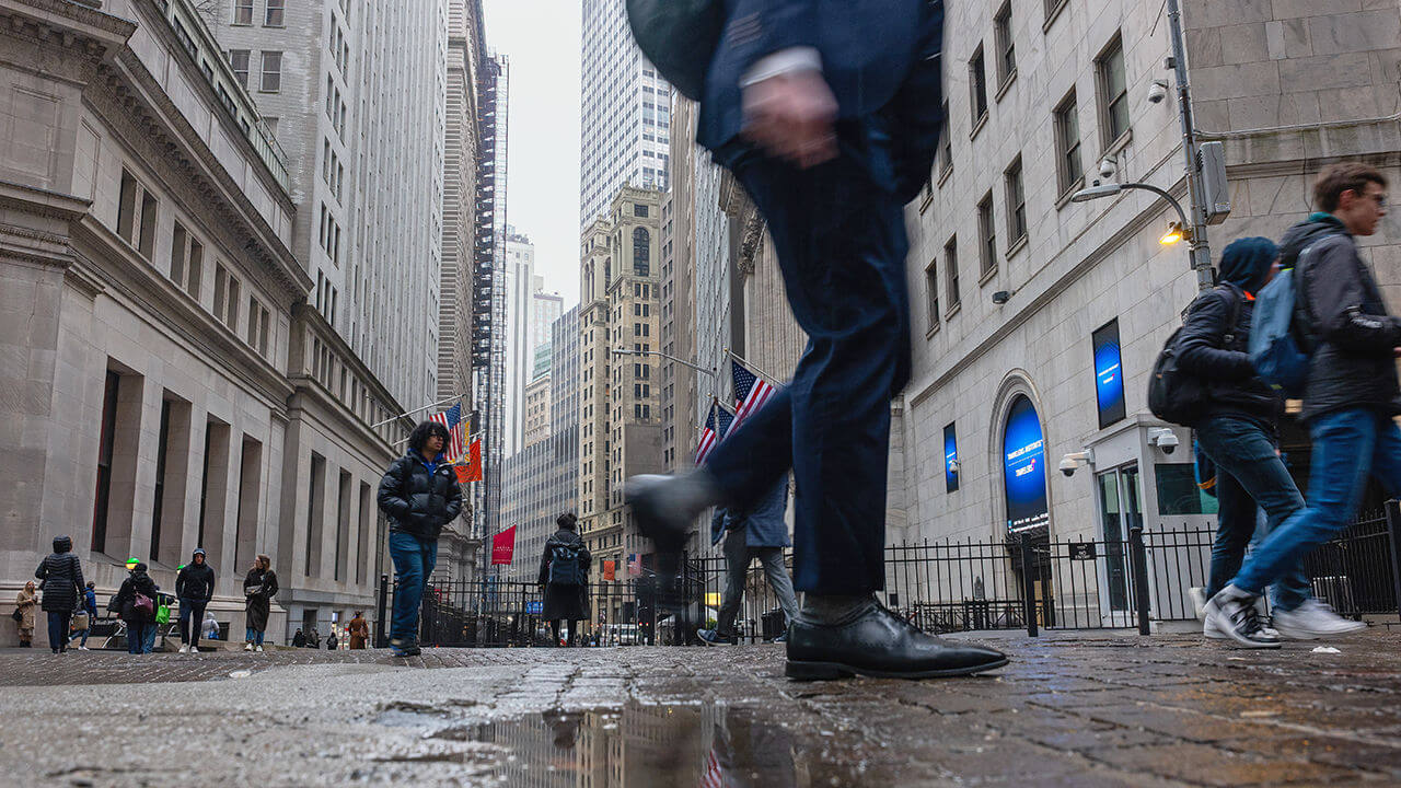People walk aong Walll Street in the rain