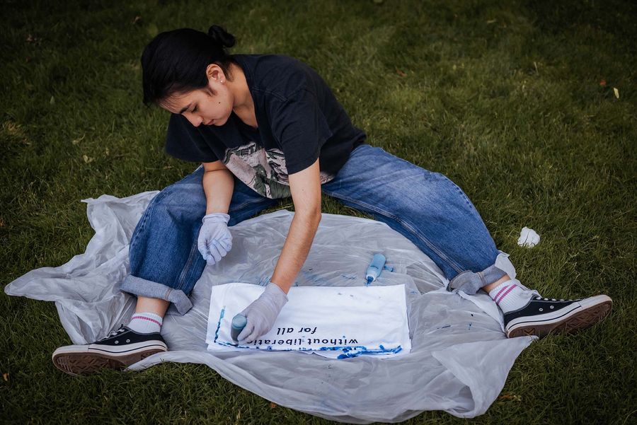 Photo: A person sitting on the grass and tie-dyeing a t-shirt at a Pride event