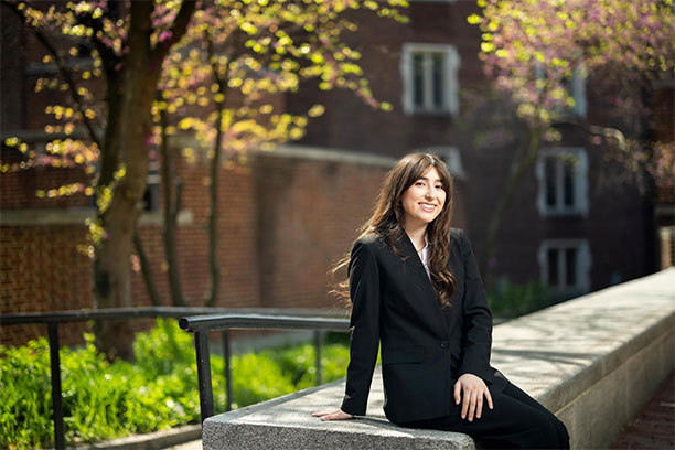 Rafaella Lambrinos sitting outdoors on Penn's campus, smiling and facing forward.