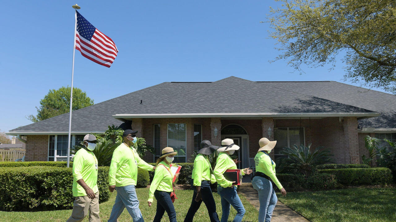 A community response team wearing fluorescent yellow jerseys make their way through a neighbourhood surveying residents. USA flag in the background.