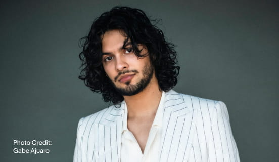 Xolo Maridueña in a white suit with dark pinstripes.