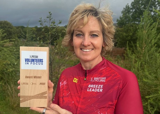 A volunteer in Breeze Leader cycling kit, holding a Volunteers in Focus award.