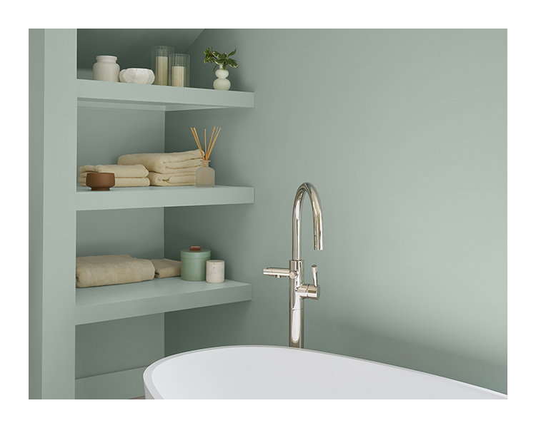 A green-gray painted bathroom with a freestanding tub and built-in shelving.