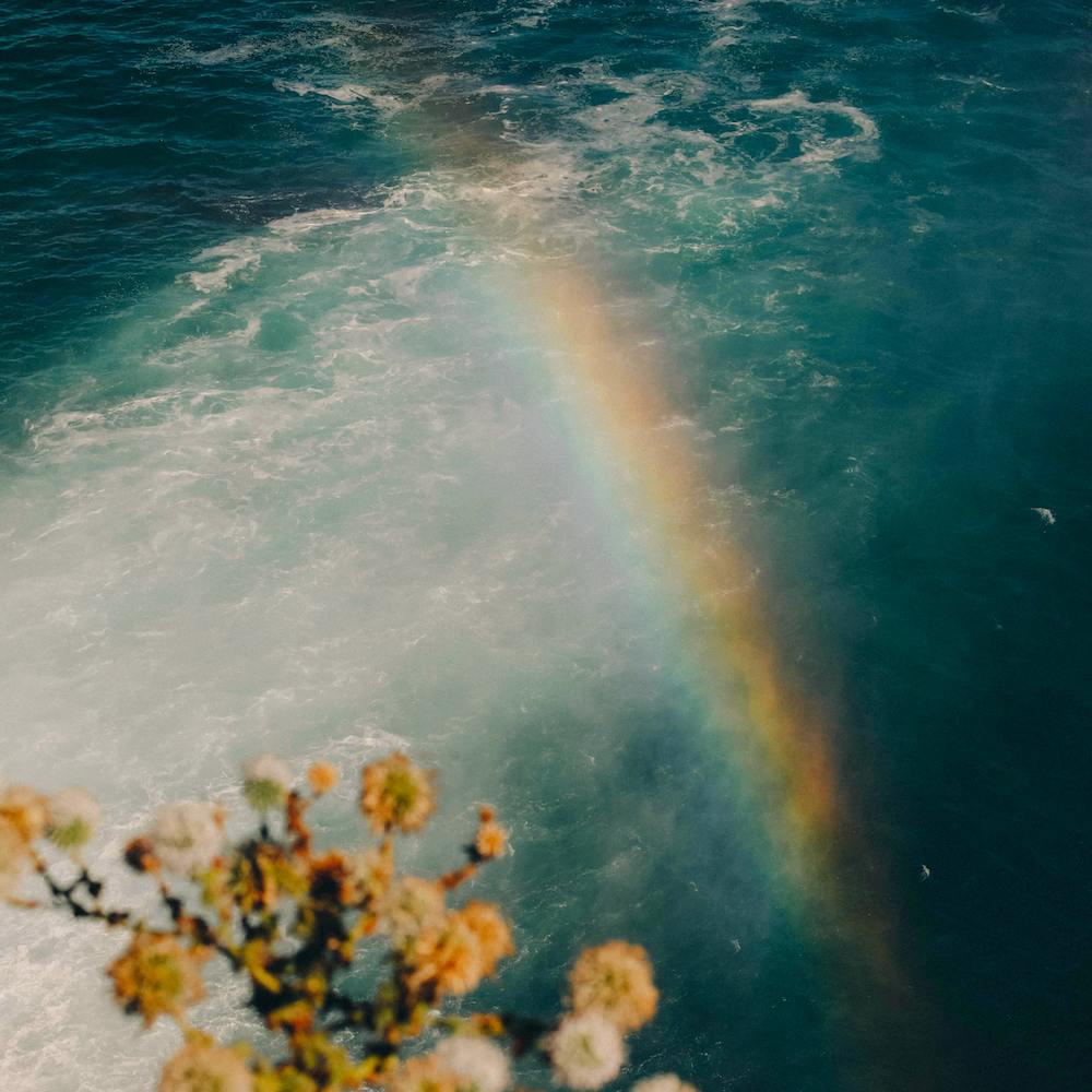 A pale rainbow hovers over green-blue water. 