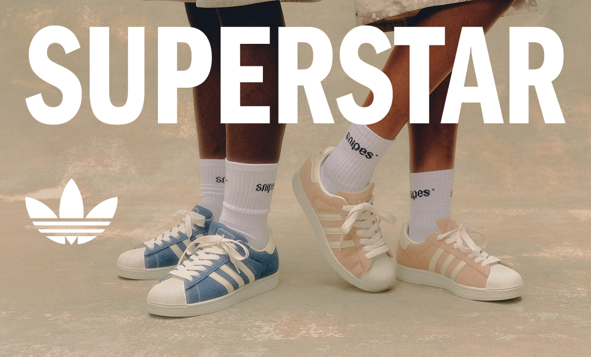 adidas Superstar Sneaker in Blau und Rosa mit weißen Socken vor hellem Hintergrund. Schriftzug „SUPERSTAR“ und adidas-Logo im Bild.