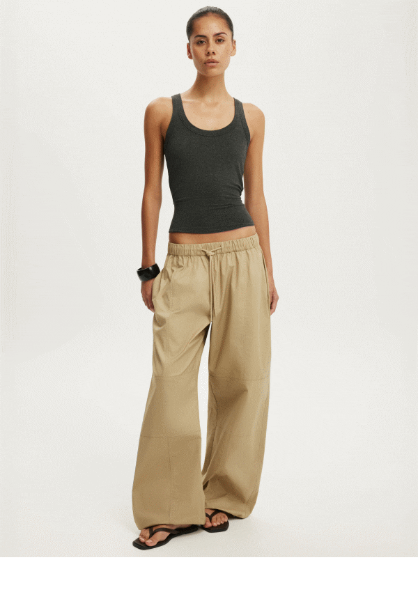 Woman wearing a charcoal gray racerback tank top and beige wide-leg pants with black slide sandals