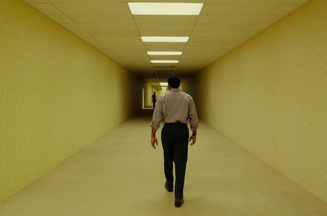 Michaela Coel stands in a dark wood room, looking at Ian McKellen, who holds a door open into a shadowed space.