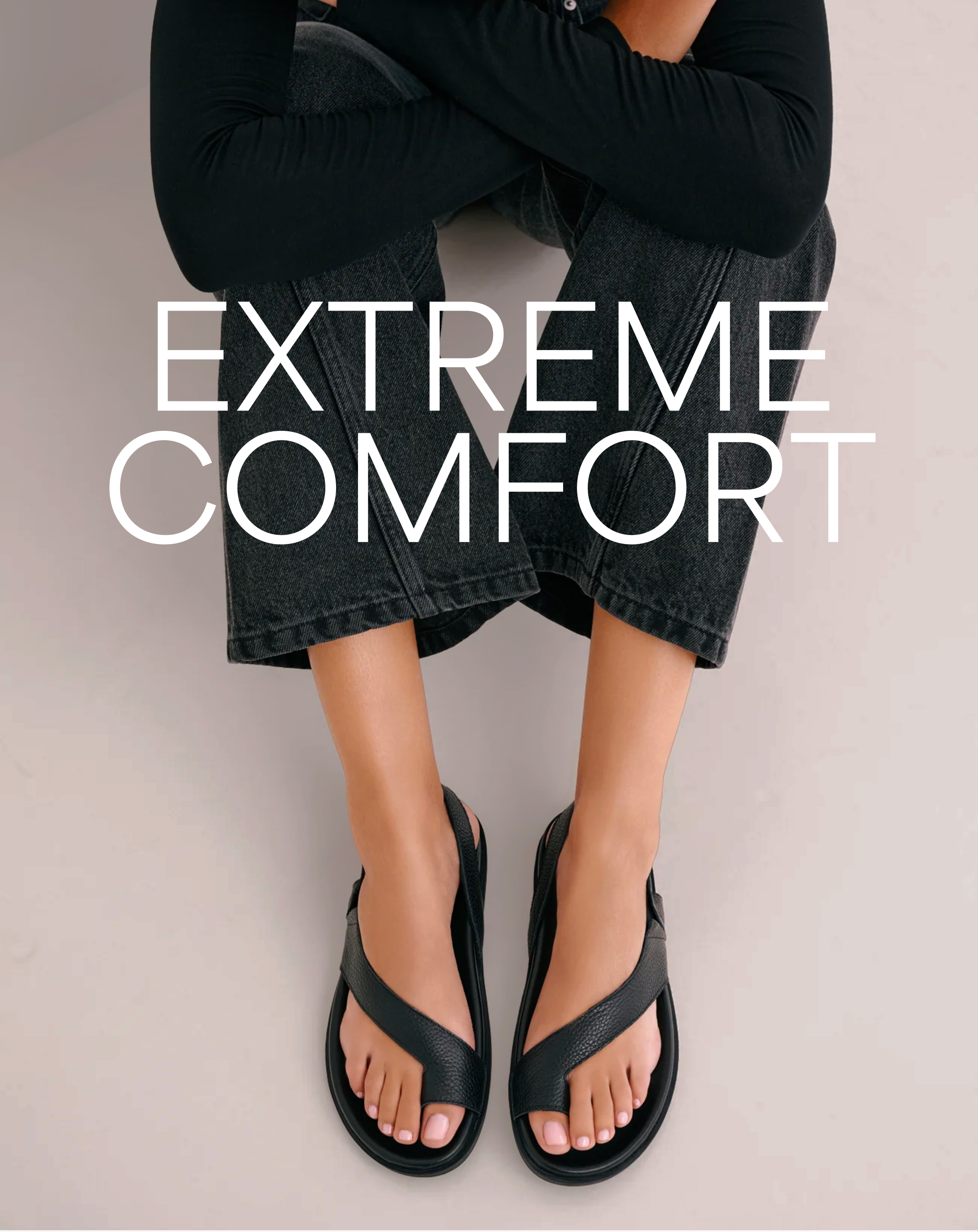 Astrid sits cross-legged in black jeans and top, wearing The Kelis Sandals with the words "Extreme Comfort" overlayed.