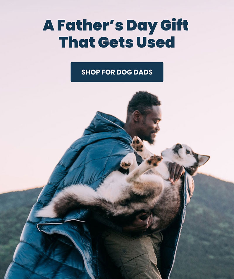 Dad carries a husky breed dog in his arms while wearing a Rumpl blanket
