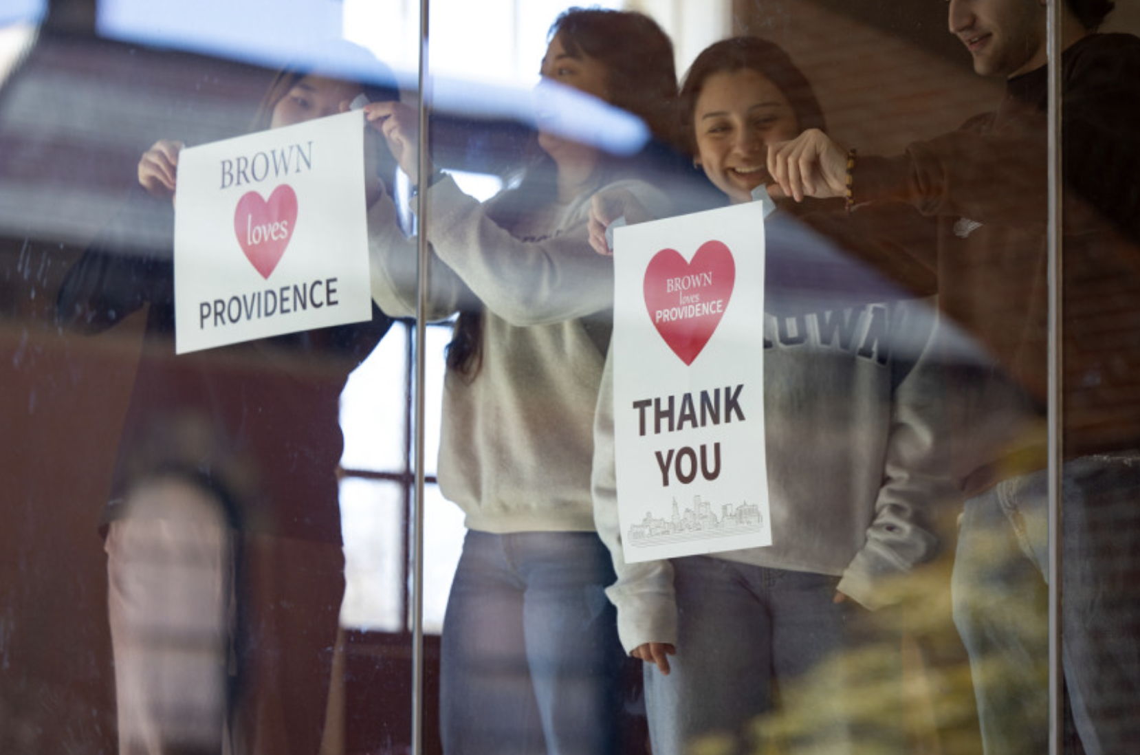 Brown students hang posters in a large window in the campus center