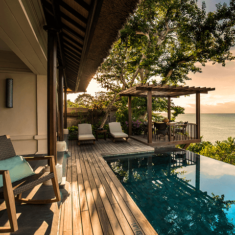 A private villa terrace with an infinity pool overlooking the ocean at sunset.