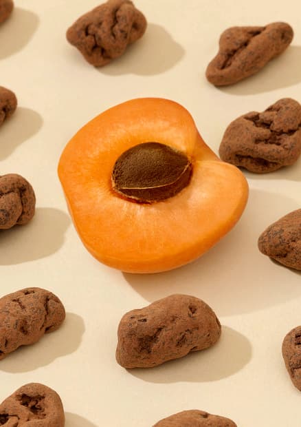 Chocolate-covered apricots next to a fresh halved apricot.
