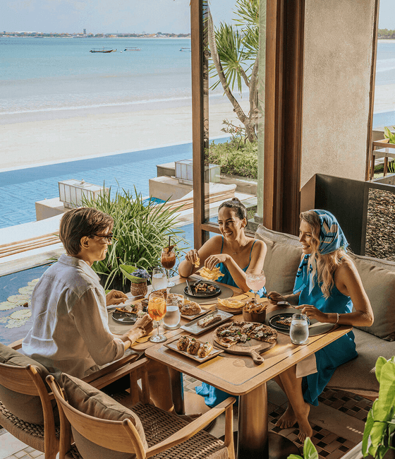 Friends enjoying a meal overlooking a beachfront pool and open ocean views.