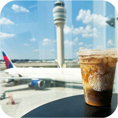 A caramelly iced coffee drink on a black table in front of an airport window with a Delta airplane outside.