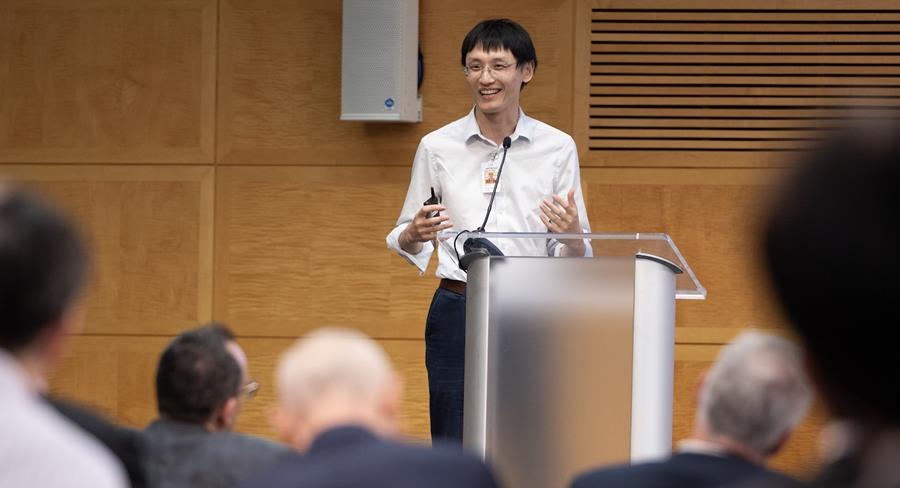 A person smiles while giving a presentation from a podium.