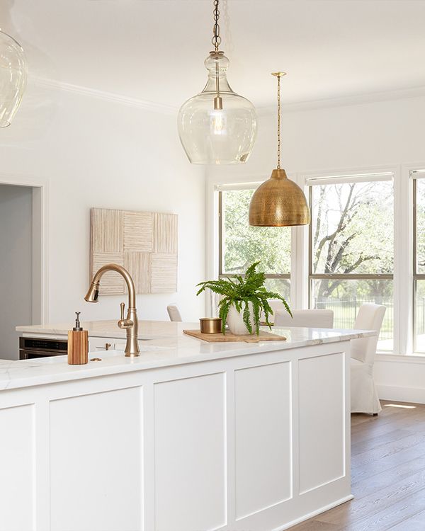 A white-painted kitchen with a large paneled island, gold hardware, and pendant lighting.
