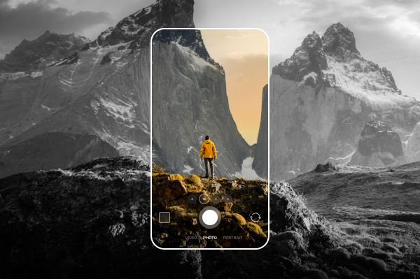 A smartphone screen showcasing a vibrant photo of a person in a yellow jacket standing on a cliff with mountains in the background, set against a black and white version of the same landscape.