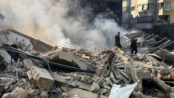 Firefighters inspect destruction as smoke billows.