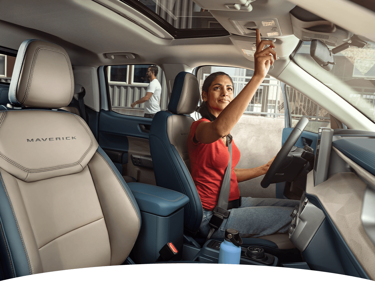 A woman turning on the dome lights of a 2025 Ford Maverick&reg; truck while sitting in the driver&rsquo;s seat