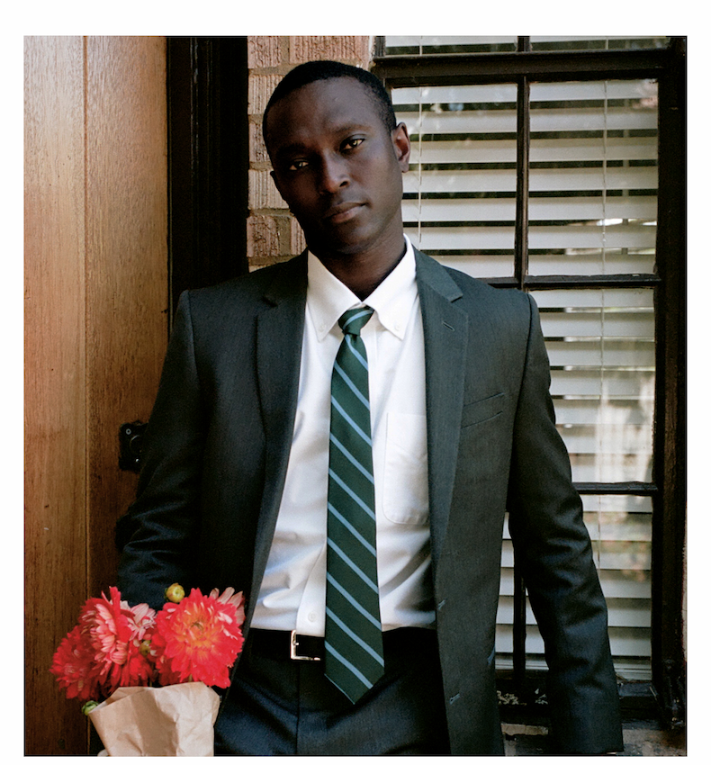  Man wearing a dark suit with a green striped tie and a white oxford shirt, holding a bouquet of red flowers.
