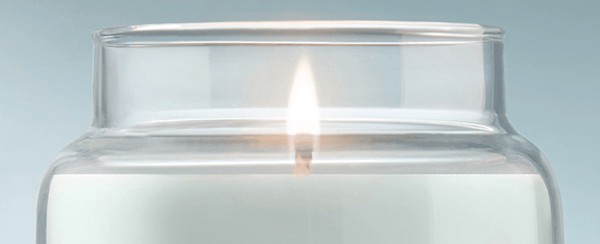 White candle in a clear glass jar with a single flame, close-up view