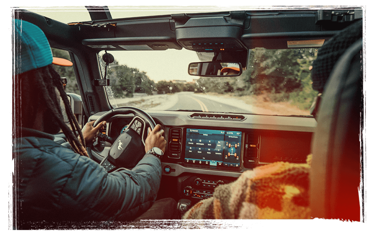 The view of the road ahead from inside a Bronco&reg; SUV, with a driver and passenger in the front seats