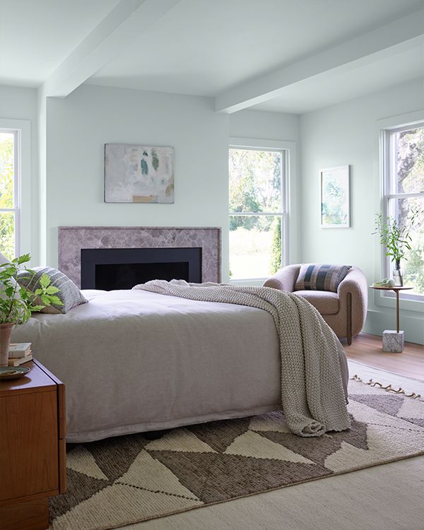 A pale blue painted bedroom with a stone fireplace, decoratve area rug, and neutral furnishings.