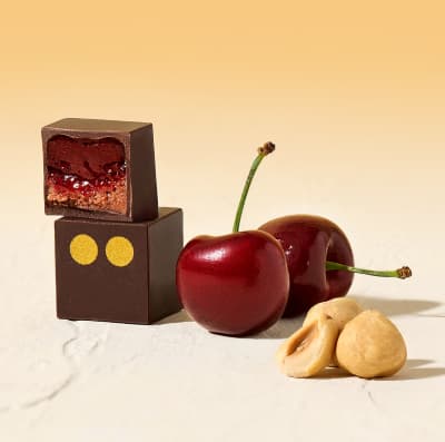 Two Cherry & Hazelnut bonbons next to some fresh cherries and hazelnuts.