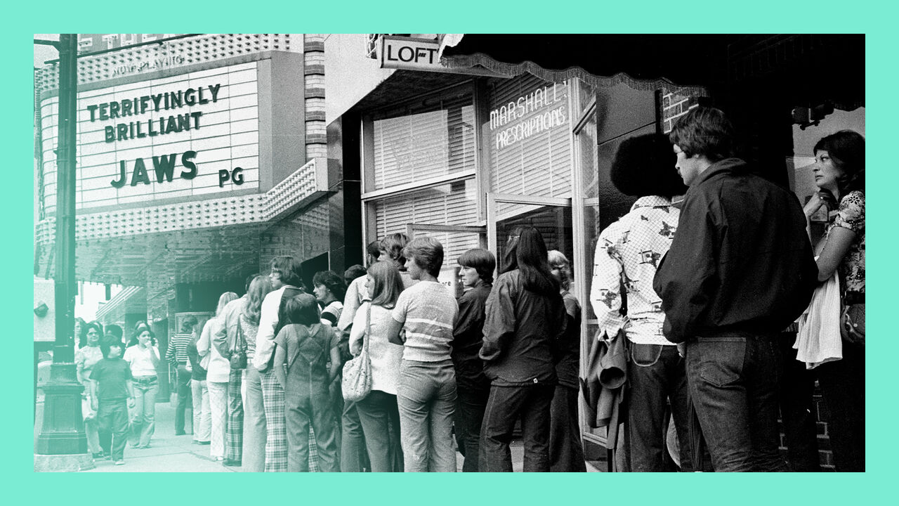 View of a line of moviegoers outside the State Theatre in Michigan on July 14th 1975. The cinema marquee advertises the film 'Jaws.'
