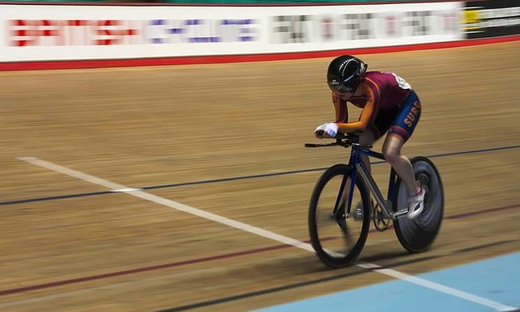 Anna rides in the time trial or pursuit position on the track in her university cycling kit.