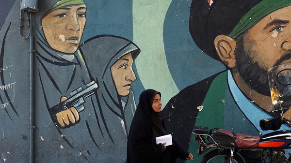 An Iranian woman walks past a wall painting of Iranian women soldiers on a street in Tehran, Iran,