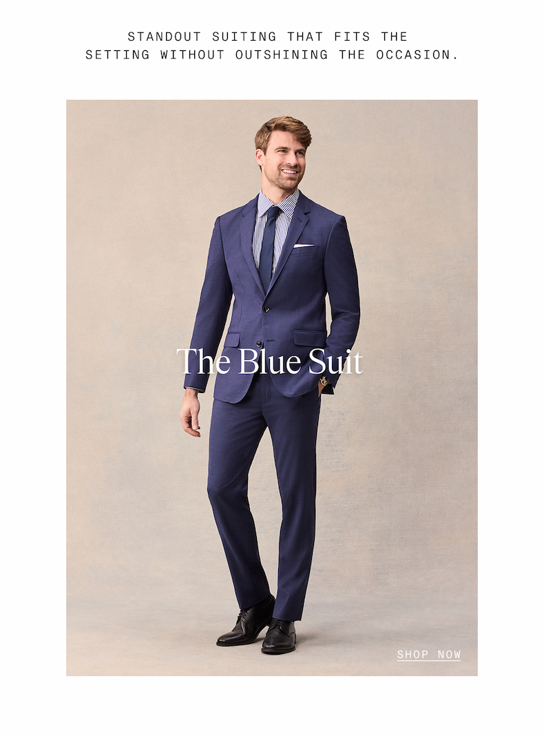 STANDOUT SUITING THAT FITS THE SETTING WITHOUT OUTSHINING THE OCCASION. Man in a navy blue suit with a striped shirt and navy tie, smiling against a neutral backdrop. The Blue Suit. SHOP NOW