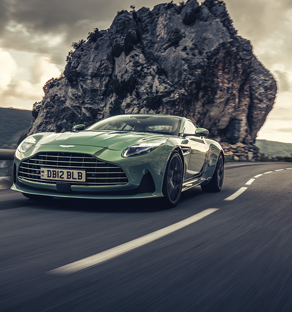 Green sportscar driving along a road with rocky mountian behind it