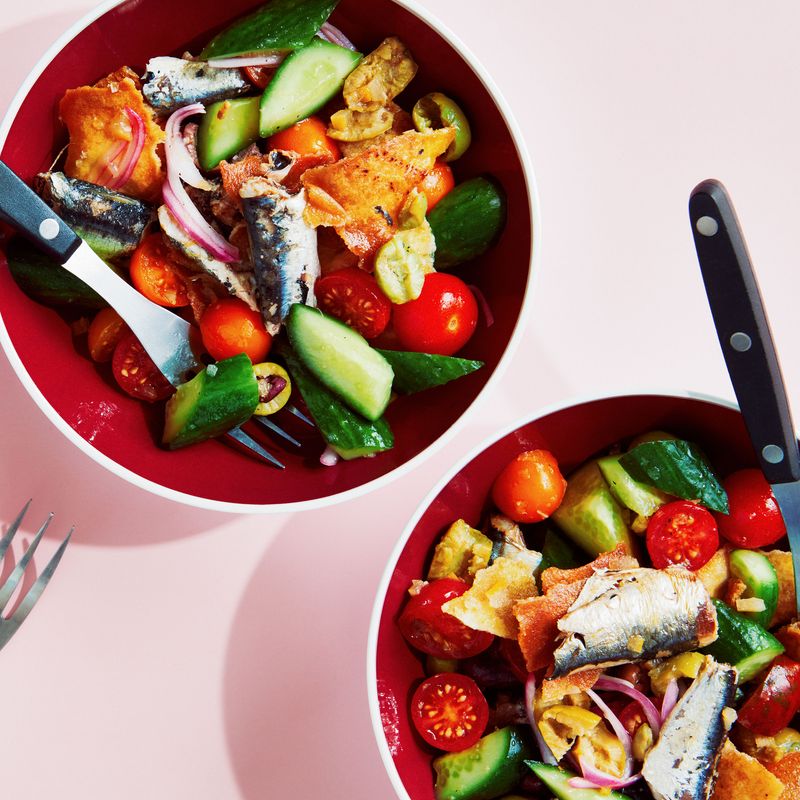 Broken up oil-packed sardines in three bowls with chopped preserved lemons, Persian cucumbers, cherry tomatoes, red onions, mixed olives, and salted pita chips.