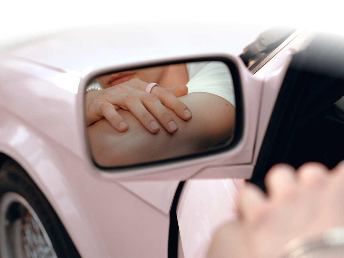 Person wearing Oura Ring 4 Ceramic Petal reflected in pink car side mirror