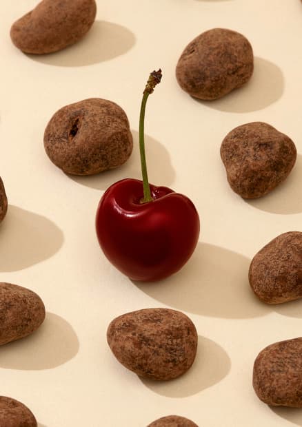Chocolate-covered Montmorency sour cherries next to a fresh cherry.