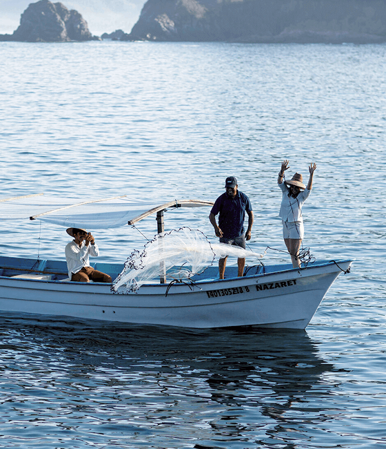 Fishermen on a boat casting nets in a calm ocean.