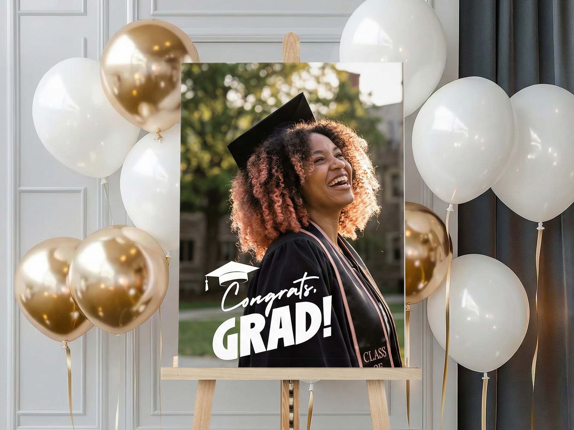 Graduation welcome sign on easel with smiling graduate photo, ‘Congrats Grad’ text, and decorative white and gold balloons