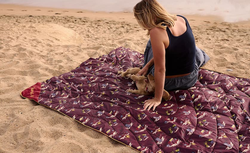 Woman and dog relax on Stash Mat on sandy beach