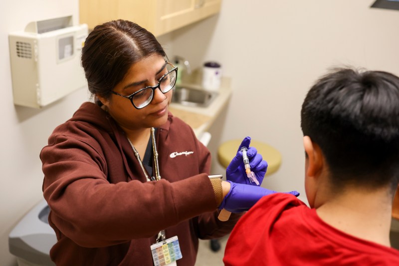 A nurse wearing gloves gives a seated patient an injection in their arm.