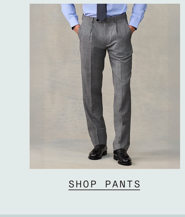 Man wearing gray pleated dress pants with a light blue dress shirt and navy dotted tie, paired with black loafers. Text: "SHOP PANTS"