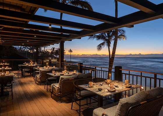 An empty restaurant balcony at night overlooking the ocean.