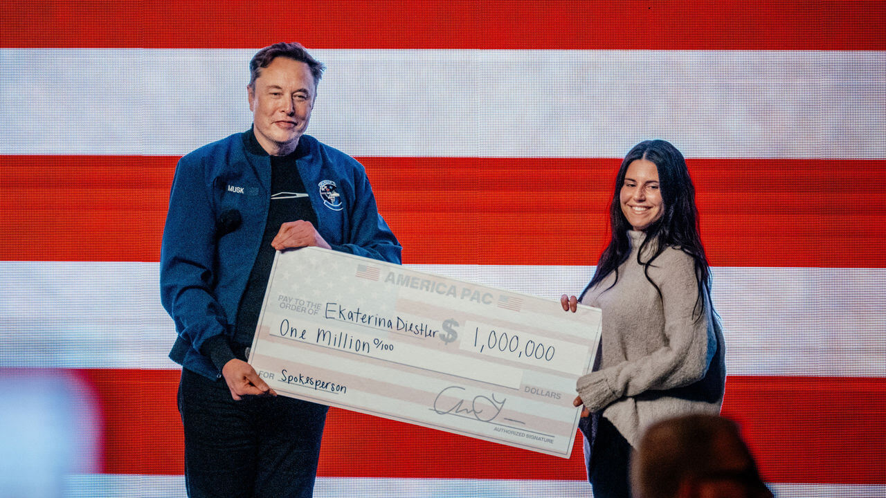 Elon Musk presents a one million dollar check to an attendee during an America PAC town hall ahead of the Wisconsin Supreme Court election at the KI Convention Center.
