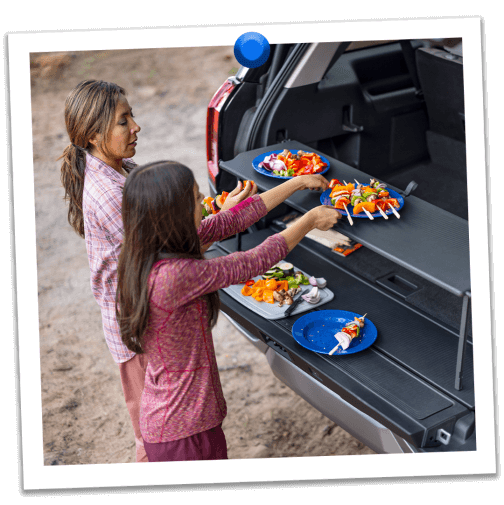 A mother and daughter prepare kebabs at their campsite on the pop‑up tailgate tabletop of their Expedition&reg; SUV 
