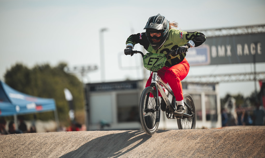 A BMX rider squats down onto their bike as they pump through a section of rollers.