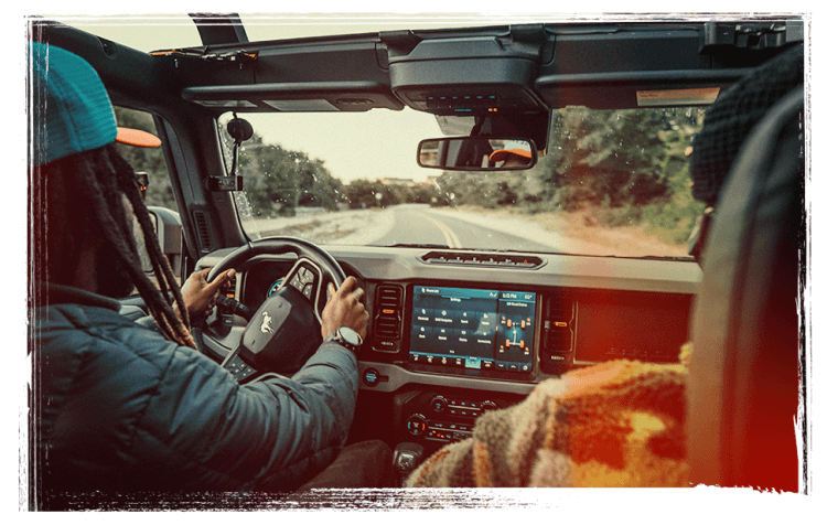 The view of the road ahead from inside a Bronco&reg; SUV, with a driver and passenger in the front seats